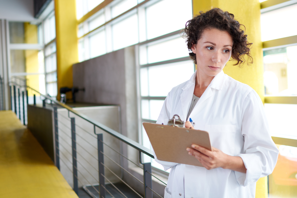 Portrait of a female doctor holding her patient chart in bright modern hospital